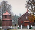 Widok na fasadę kościoła oraz drewnianą dzwonnicę. Teren przykościelny otaczaja drzewa.