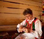 Pani Wiesława siedzi w wiejskiej izbie i wycina wycinankę. Za nią święty kąt z krzyżem i bukietami z bibuły.
