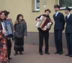 Grupa przebierańców na ulicy w Jedlińsku. Dwóch chłopców przebranych jest za policjantów w mundurach. Inni grają na akordeonach, Są też chłopcy w przebraniach kobiet.