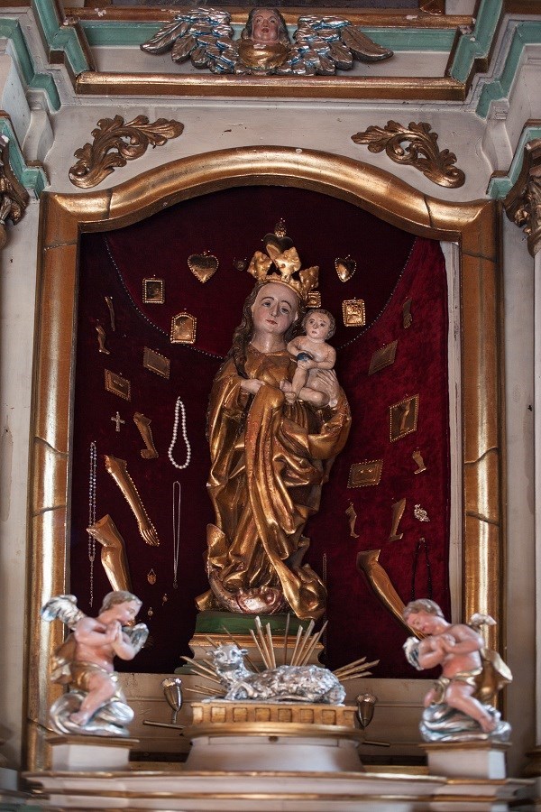 Figura Matki Bożej z Dzieciątkiem w ołtarzu głównym. U stóp Matki Boskiej Baranek Boży (agnusek). Po jego bokach widzimy dwa aniołki. Figurę otaczają dary wotywne.