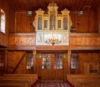 Zdjęcie przedstawia chór wraz z organami. Ściany i strop oszalowane deskami.