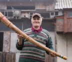Eugeniusz Szymaniak stoi na swoim podwórku. W rękach trzyma ligawkę. Za nim zabudowania gospodarcze z gołębnikiem.