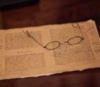 Pożółkła kartka z książki z odręcznymi notatkami Koberga. Na kartce leżą okulary w drucianych oprawkach.