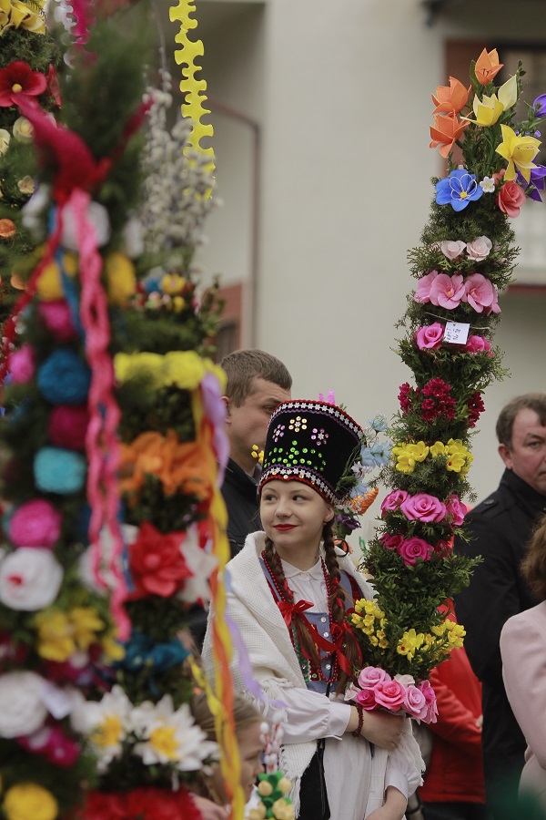 Uczestnicy Niedzieli Palmowej. Ujęcie jest skierowane na dziewczynkę w stroju ludowym trzymającą palmę wielkanocną.