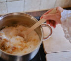 Kucharka miesza w garnku skarmelizowany cukier ze śmietaną. Widzimy tylko rękę osoby gotującej.